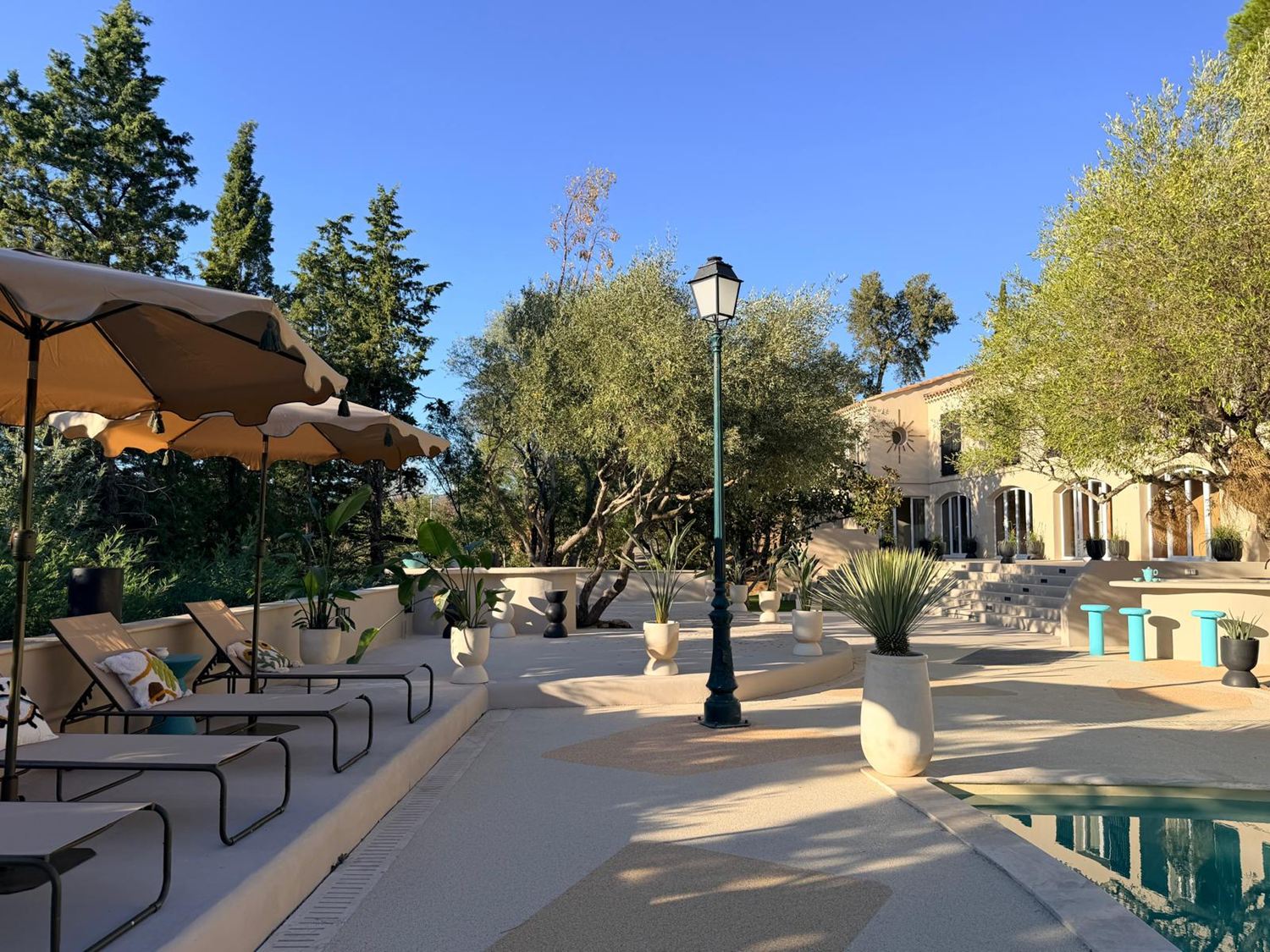 Terrasse en pierre claire avec transats, parasols festonnés et oliviers